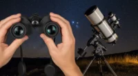 Dupla de mãos segurando um binóculo guia com telescópio ao lado, apontados para o céu estrelado, destacando telescópio vs binóculo guia